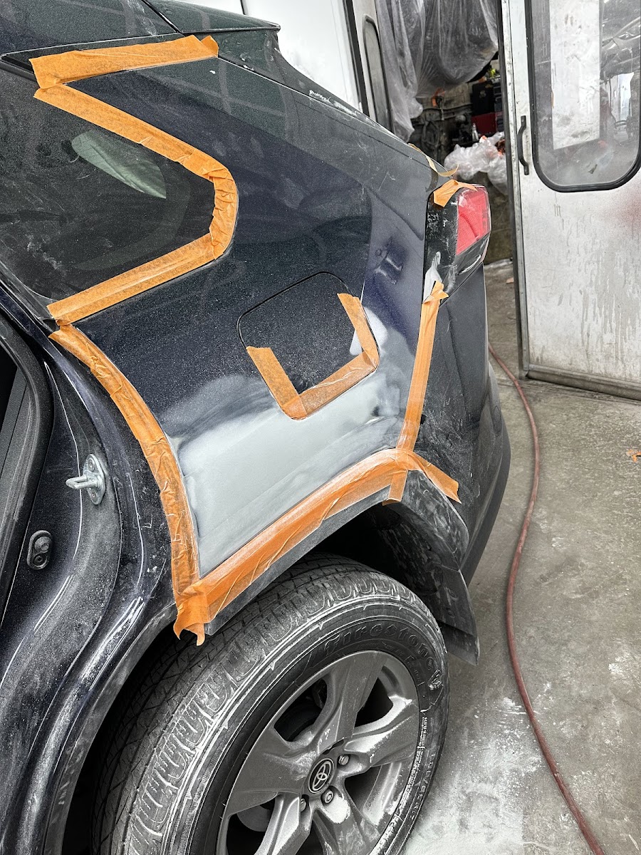 Vehicle masked in orange tape, body filler and primer applied along the rear quarter panel